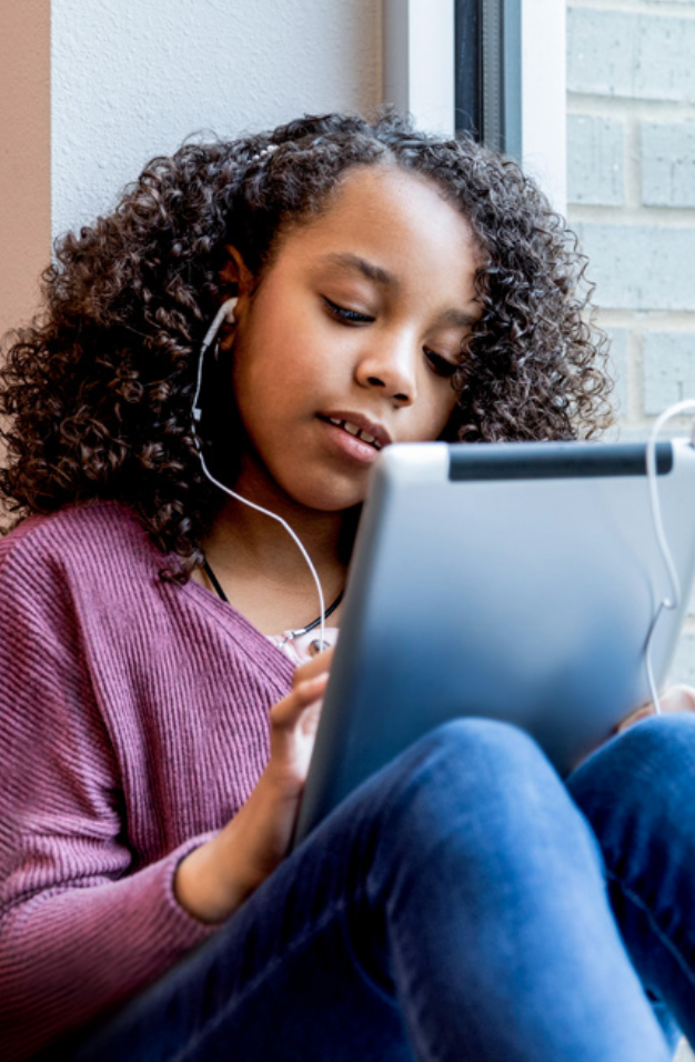 A child using a tablet device with earphones plugged in.
