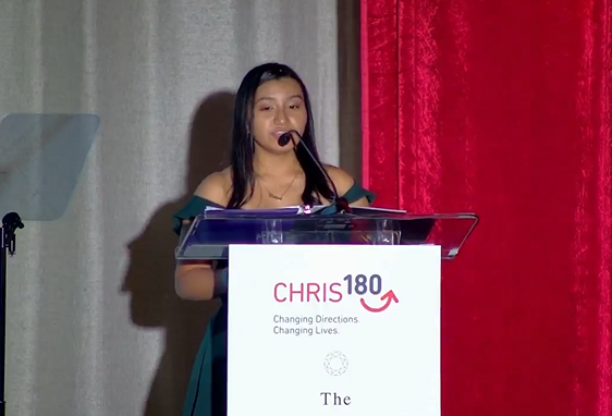 A person speaking at a podium. "CHRIS 180" sign in front.