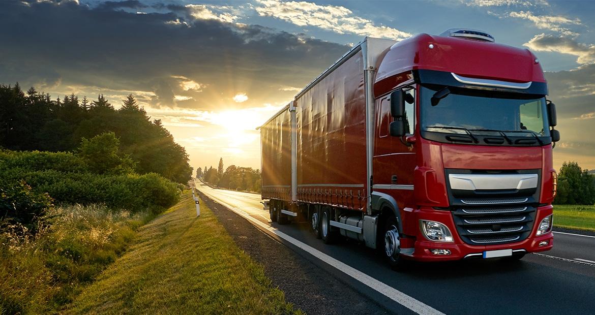 A semitruck driving down a road. A sunset in the background.