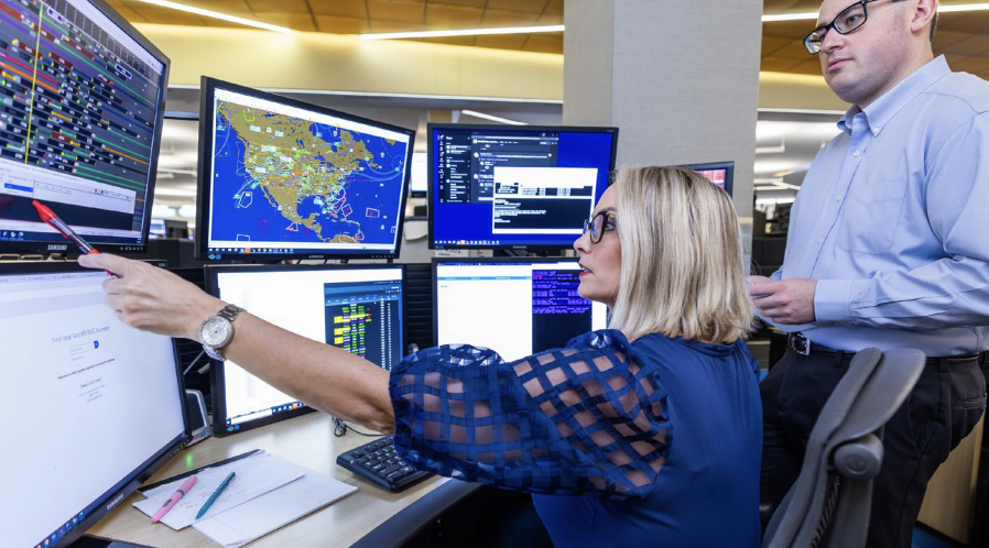 Two people looking at multiple computer monitors 