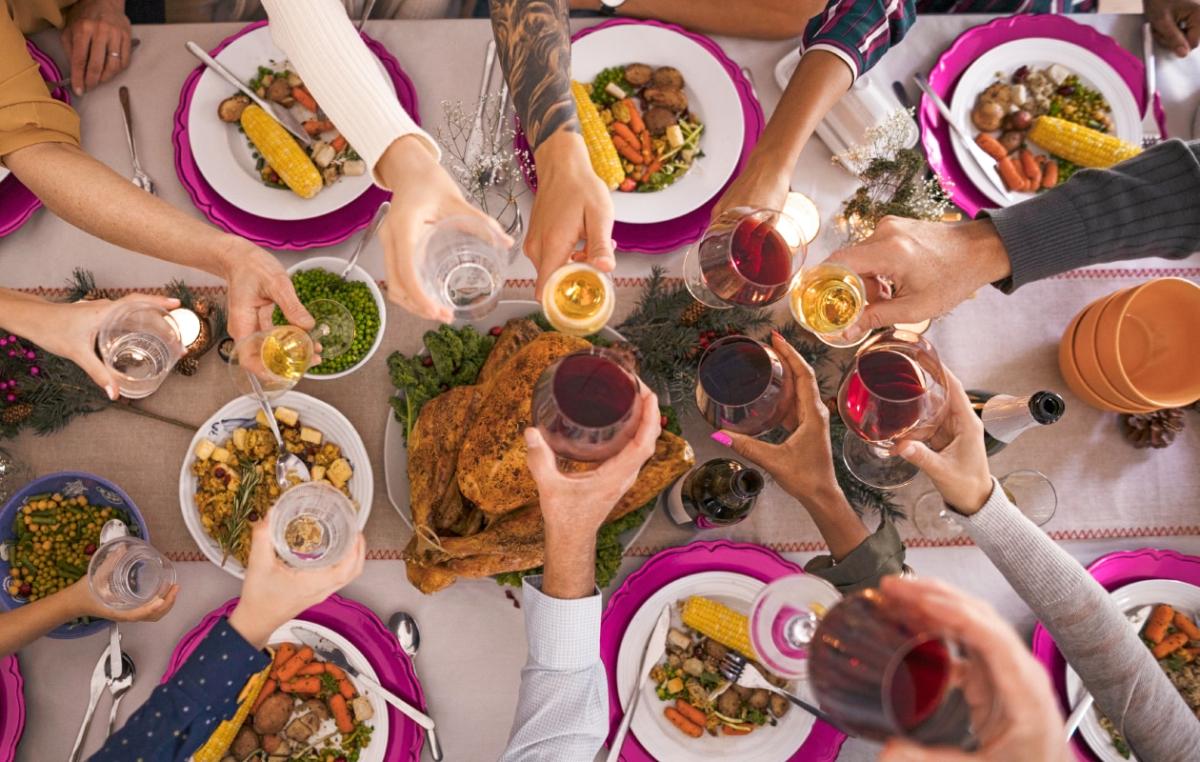 Many hands, each holding a beverage glass, meeting at the center of a table full of different foods.