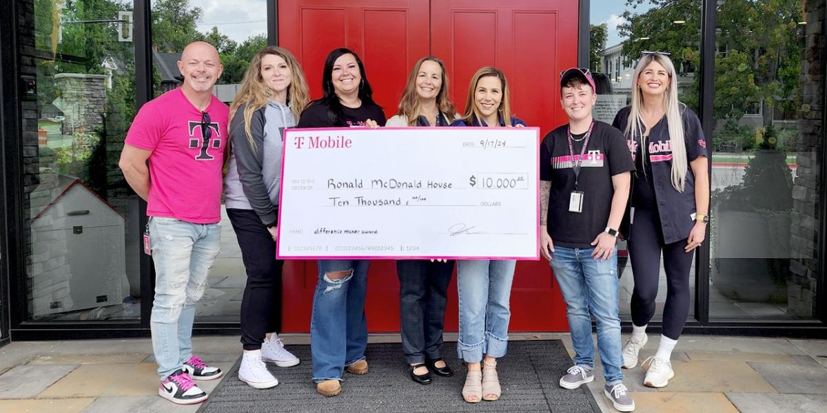 A small group posed with a large check outside a building