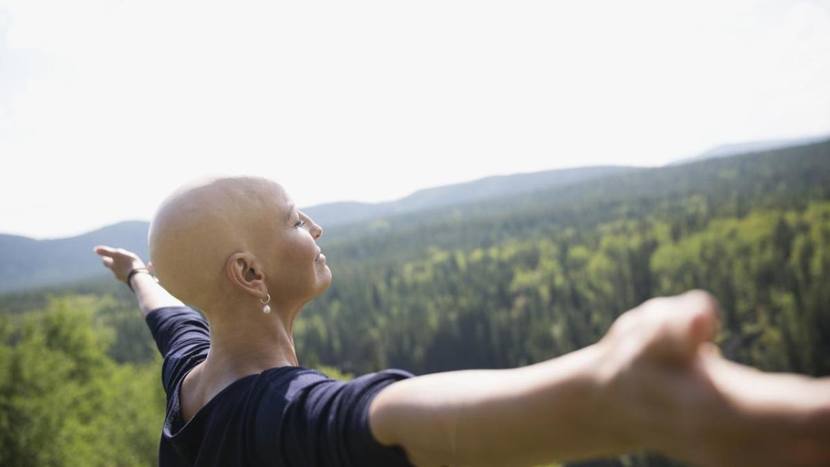 Female cancer patient shown in a field with her arms raised.