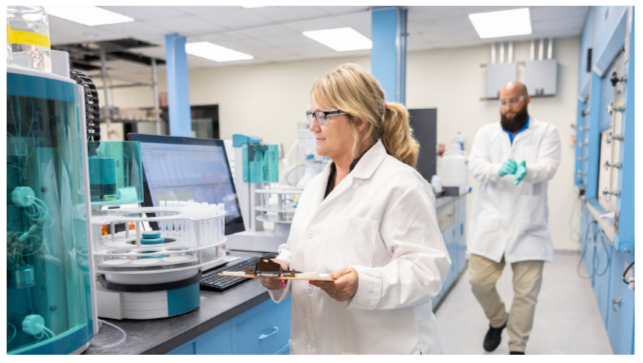 People working in a lab setting, wearing protective clothing.