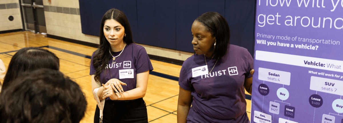 Two Truist employees talking to students in a gymnasium. A display board to the side.