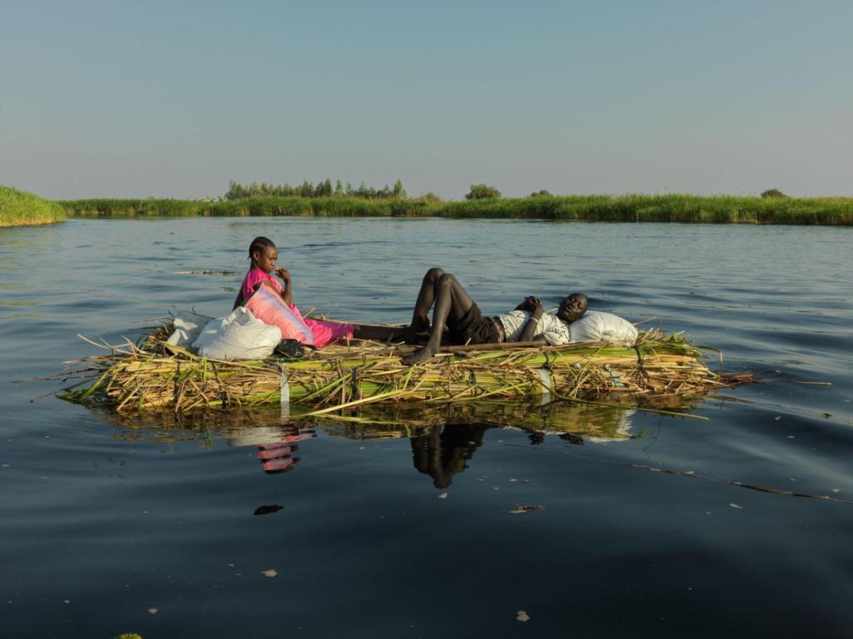 A man and wife float down the White Nile on a grass mound. They hope to reach New Fangak with the current of the river.