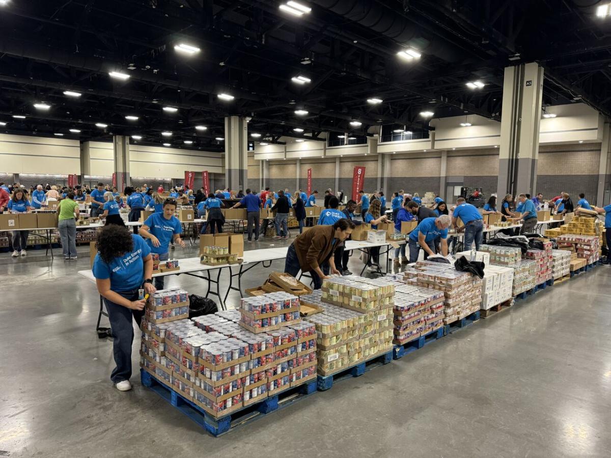 In a large warehouse, volunteers stacking pallets and containers of food.