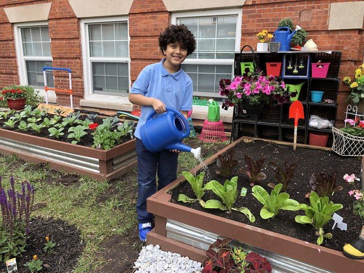 A smiling child watering plants in a raised garden bed.