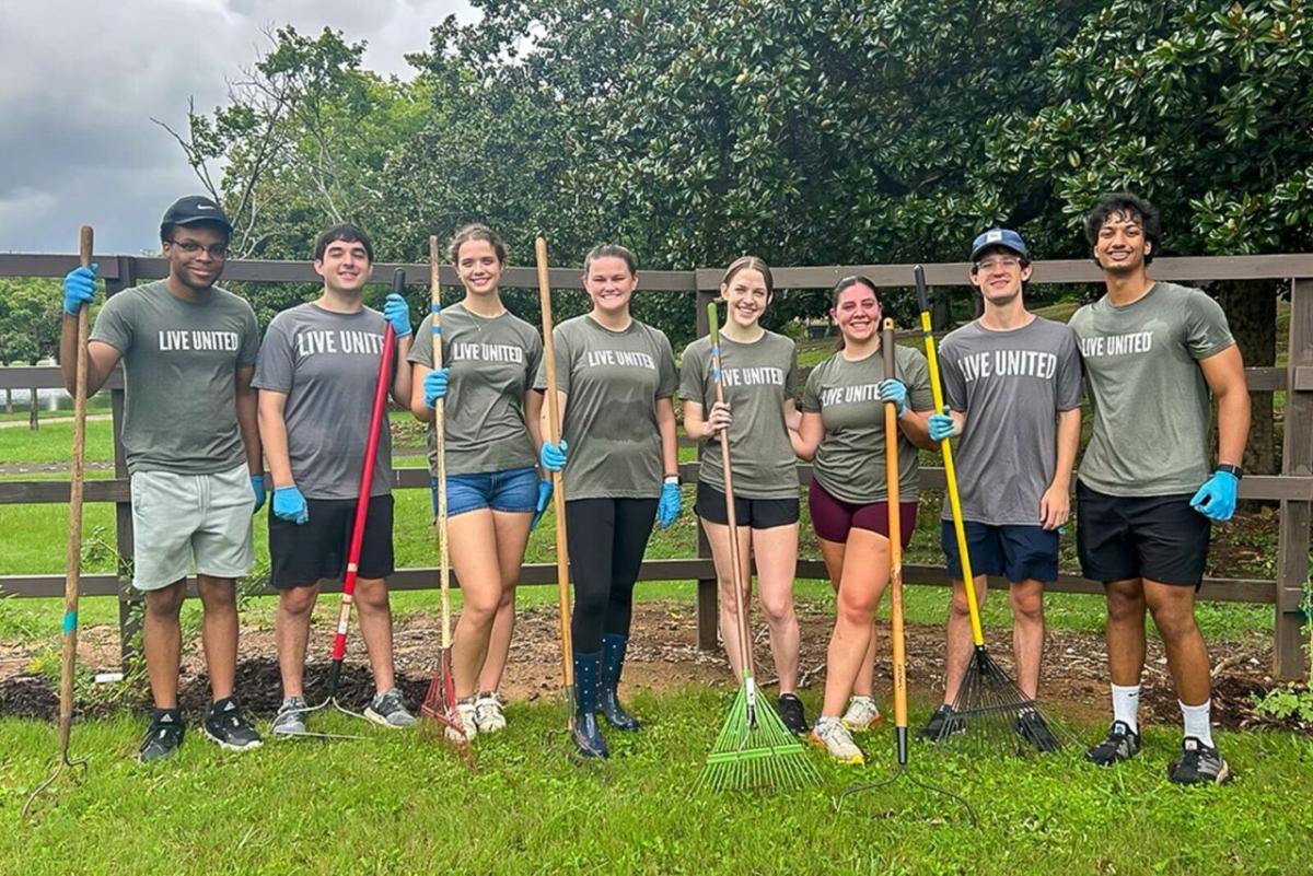 A group of volunteers posed in front of a fence with garden tools.