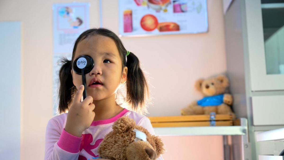 A child holding a tool to cover one eye. Holding a teddy bear with the other hand.