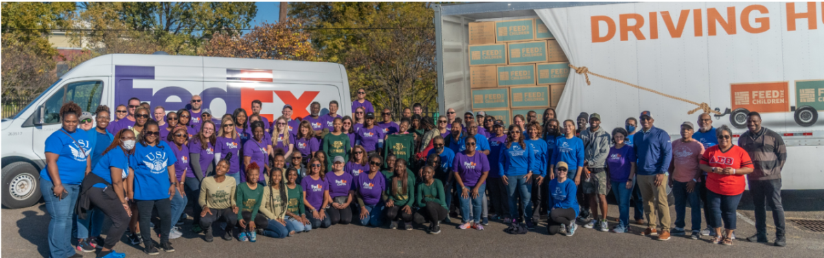 A large group of volunteers posed in front of a FedEx truck and trailer.