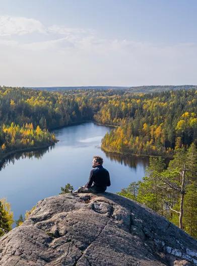 A person sitting on a rock, overlooking a scenic landscape of forest and water.