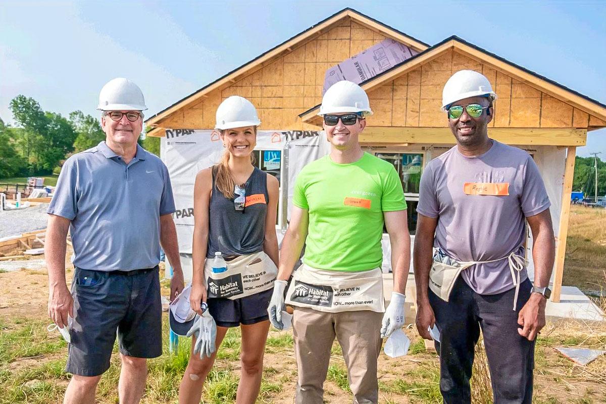 Four people posed outside a home being built