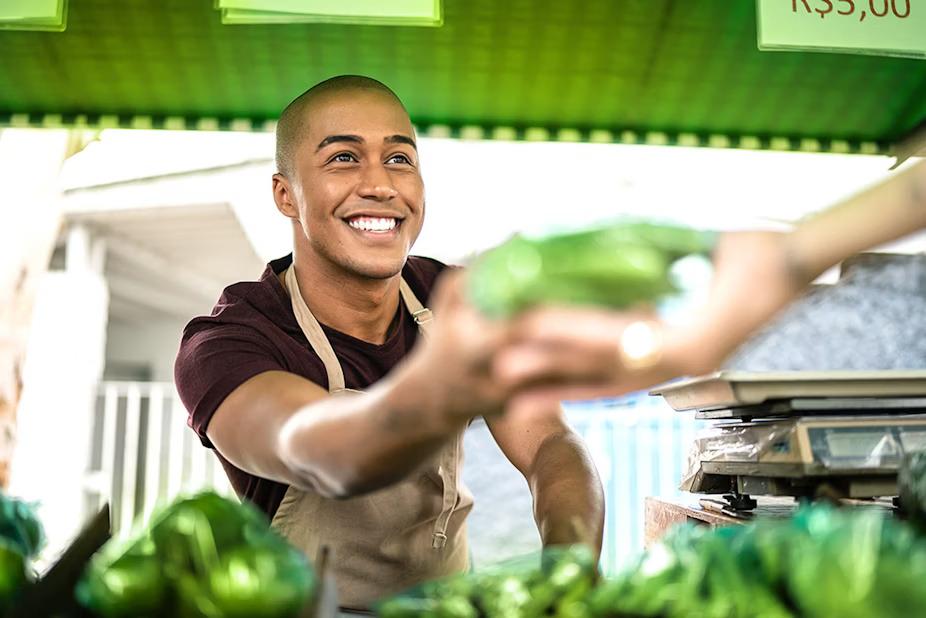 A smiling person in an apron handing something green to another.