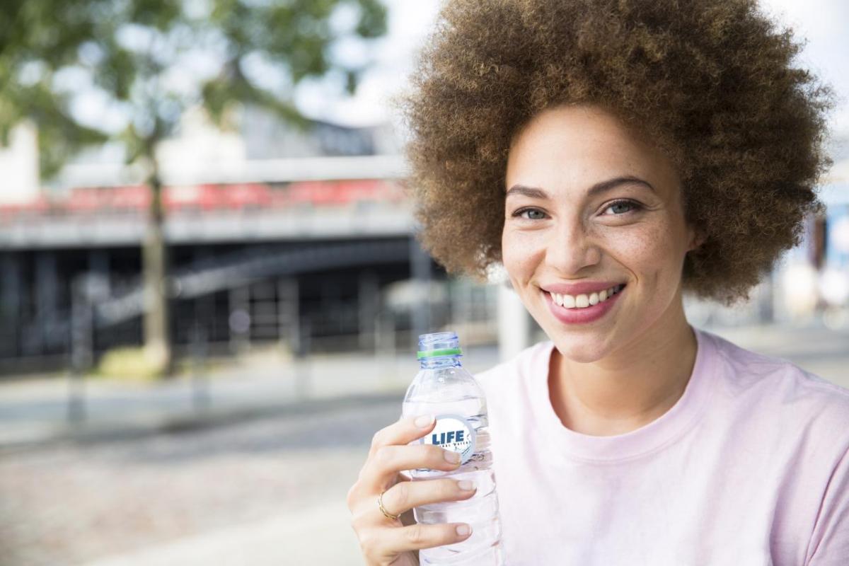 A smiling person holding a plastic bottle outside.