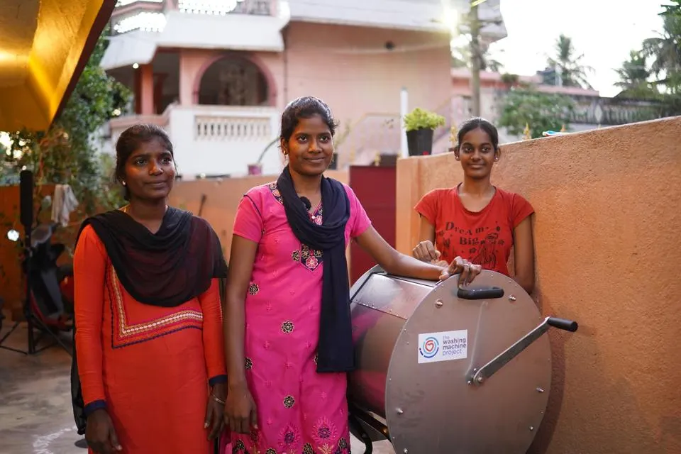 Three people standing next to a washing machine