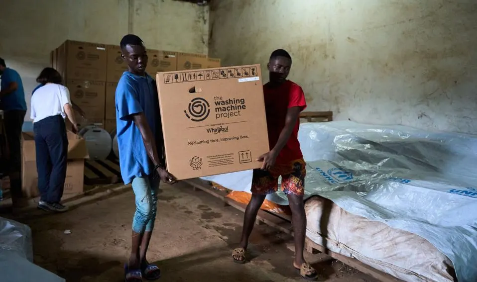 People carrying a box labeled "The Washing Machine Project"