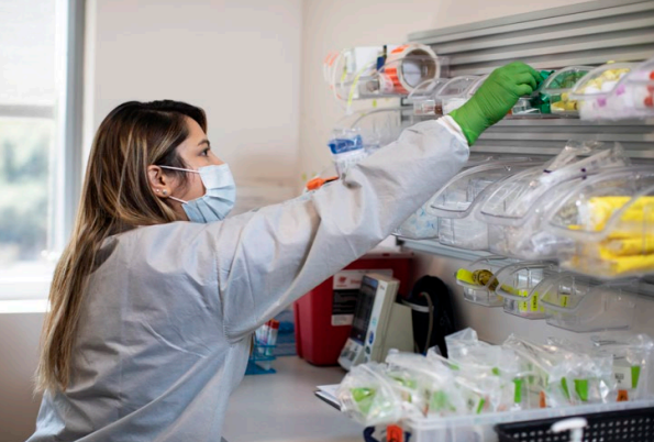 A person in protective lab gear reaching for a vial.