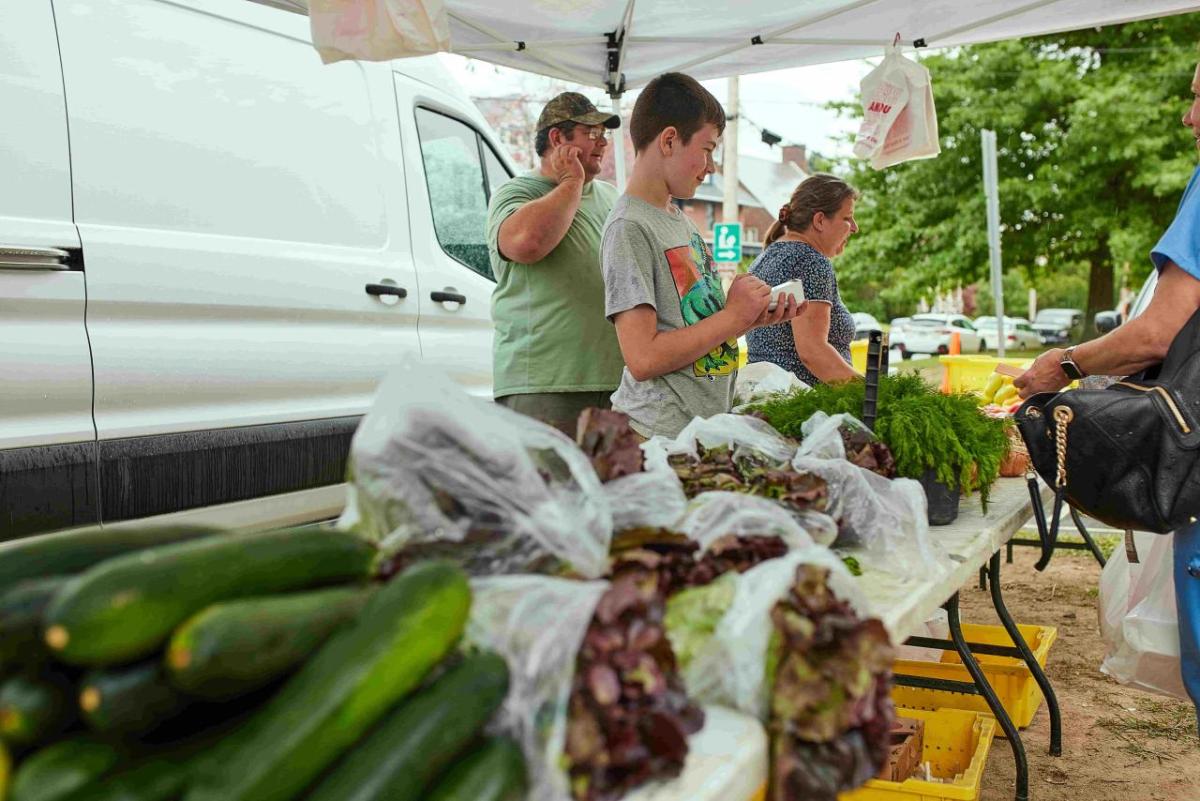 People under a tent behind tables with fresh vegetables on them