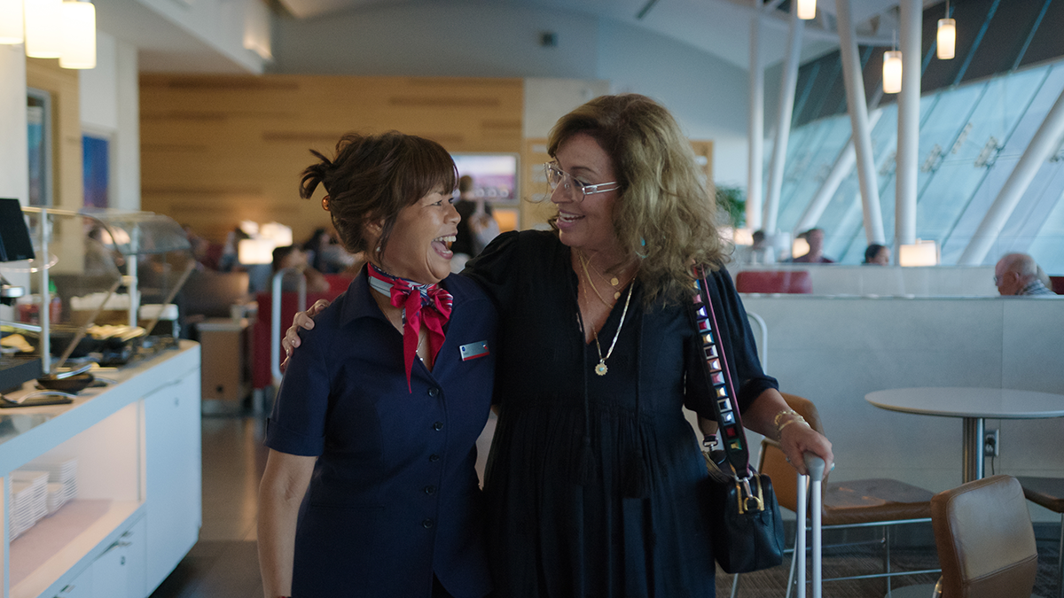 Two people walking arm in arm and looking at each other, in an airport and smiling