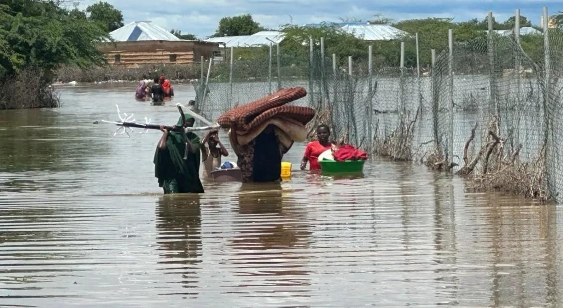 People walk through wasit-deep water, carrying belongings such as blankets