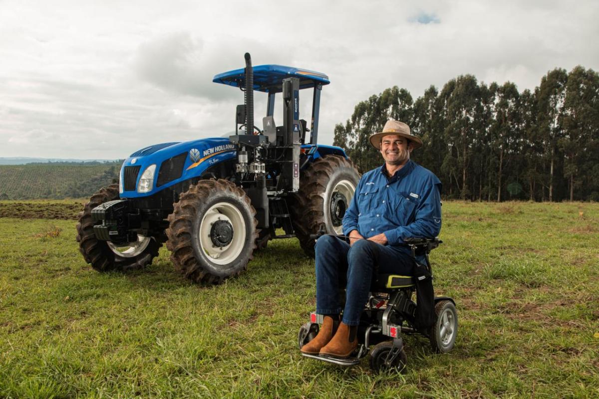 A person in a wheelchair in front of a New Holland tractor in a field.