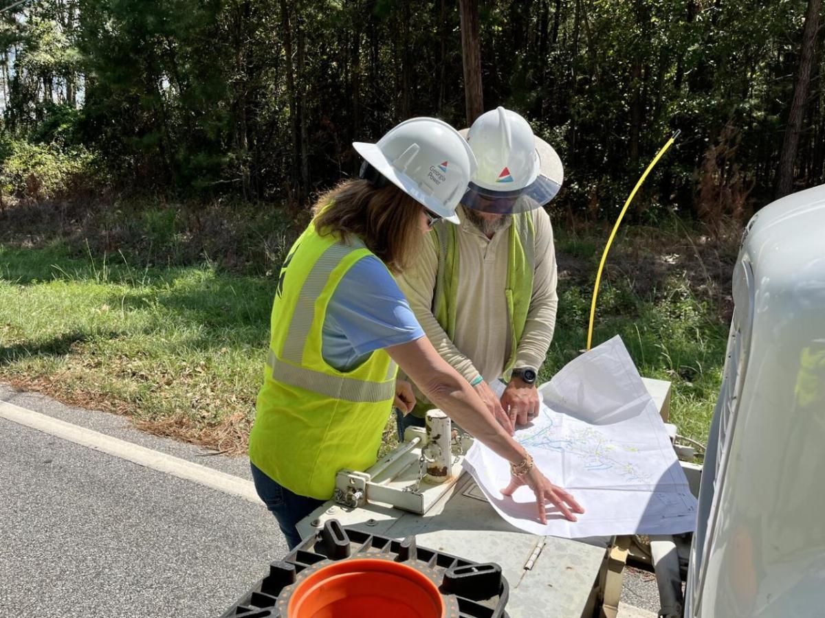 Two people in hard hats looking over a map on a table in front of a truck outside