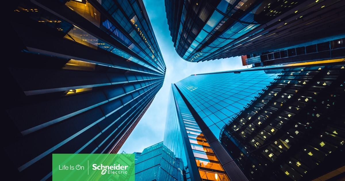 Looking up from the ground to the sky, surrounded by tall buildings close together. Schneider Electric logo at the bottom.