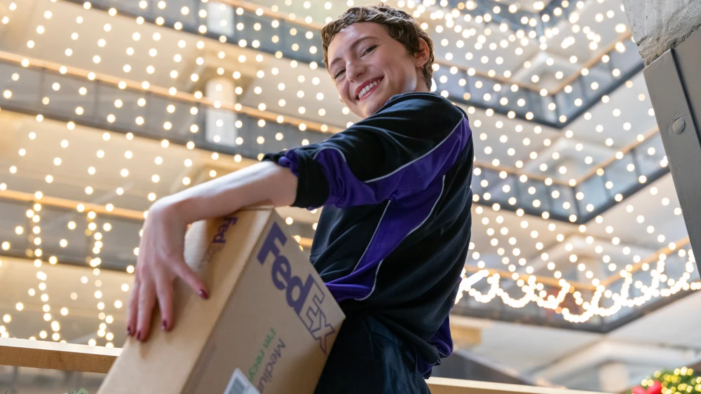 A person carrying a FedEx box, with a background of string lights