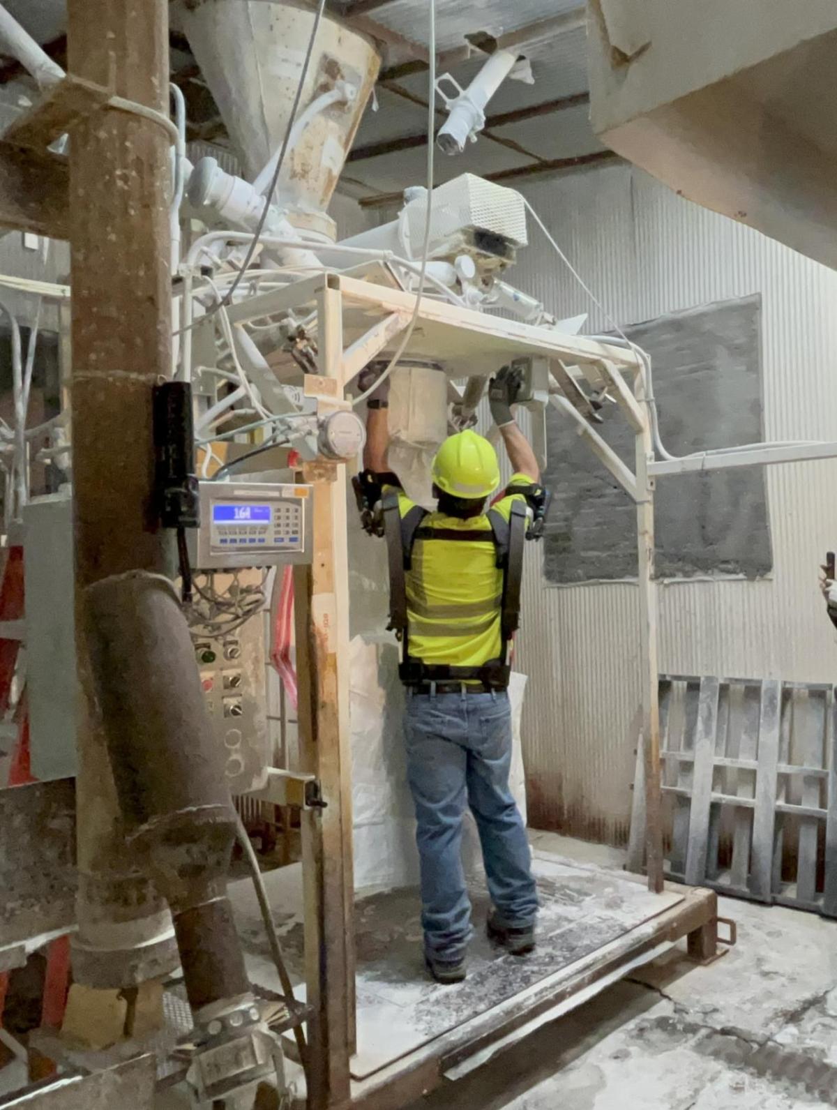 A person in protective gear in a manufacturing area, performing a repair.