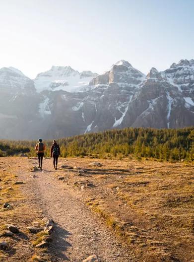 Two people walking away on a dirt path in a mountainous, scenic area.