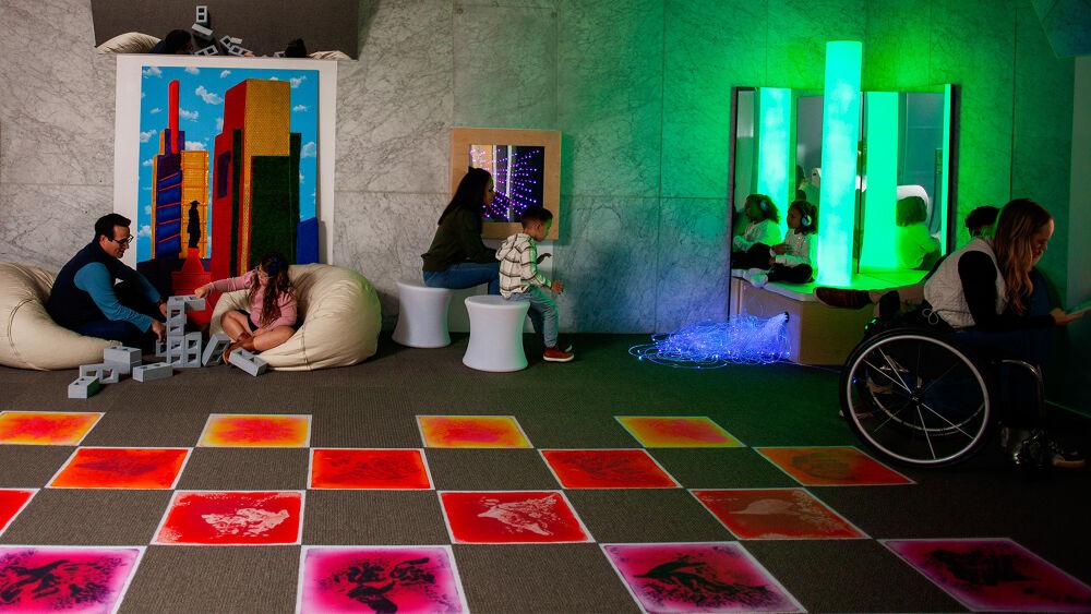 Inside the sensory room. Color changing floor tiles, a bubble tower in the corner and families playing.