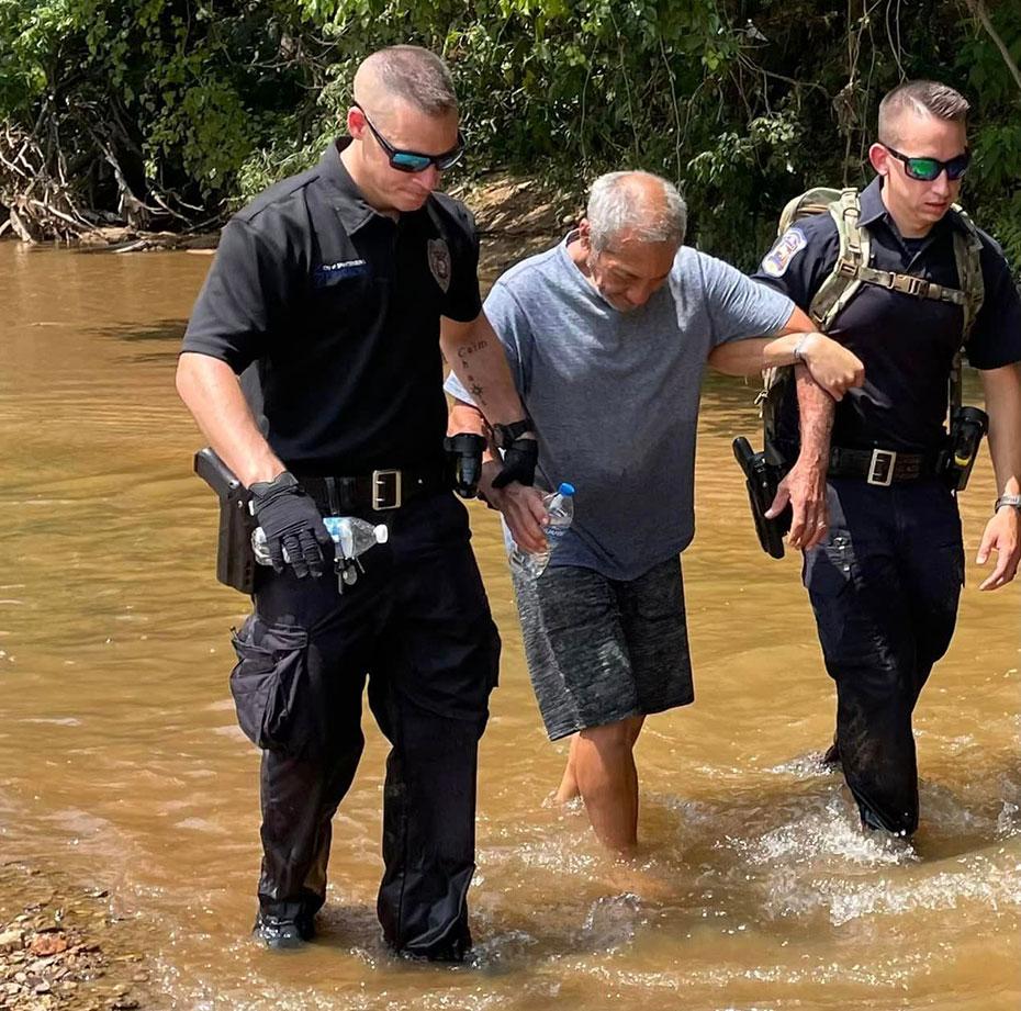 Two police officers helping a person walking through water.