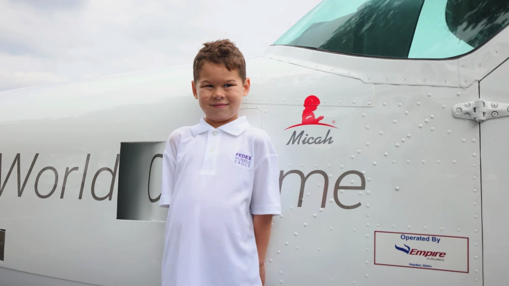 Micah next to an airplane on the ground that shows his name on the side