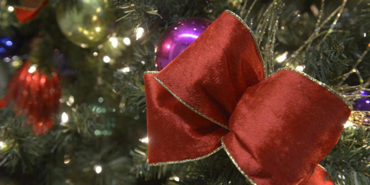 A red ribbon shown on a holiday tree with lights and ornaments