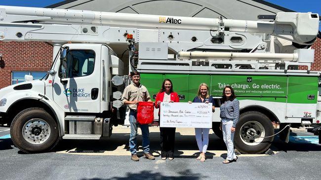 Four people standing in front of a Duke Energy truck, holding a large check