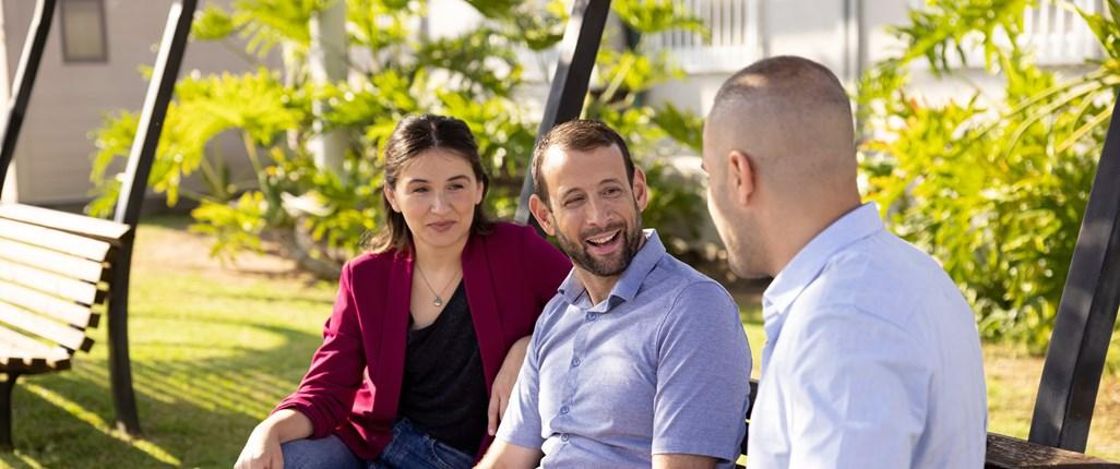 Three people talking, seated on a park bench