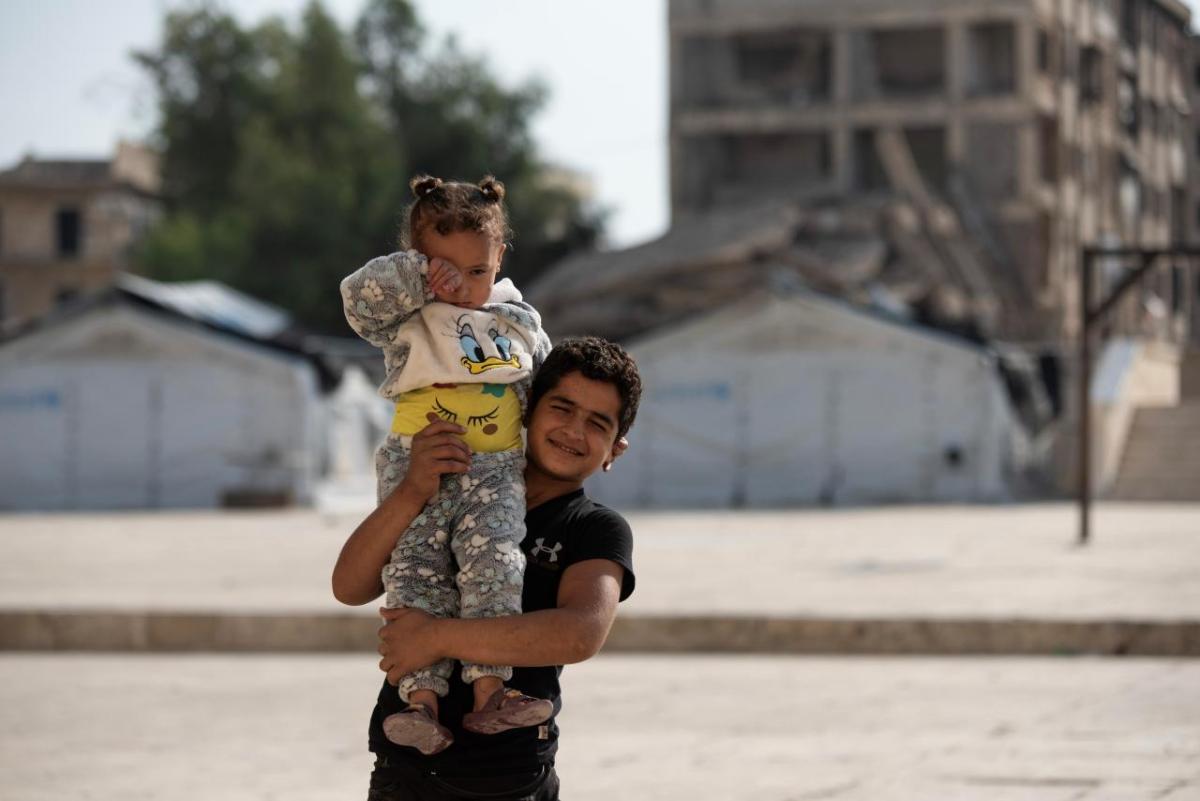 Ahmed *, 8, one of the children who live in the shelter supported by Action Against Hunger, carrying his sister in the back yard of the shelter in Aleppo. 