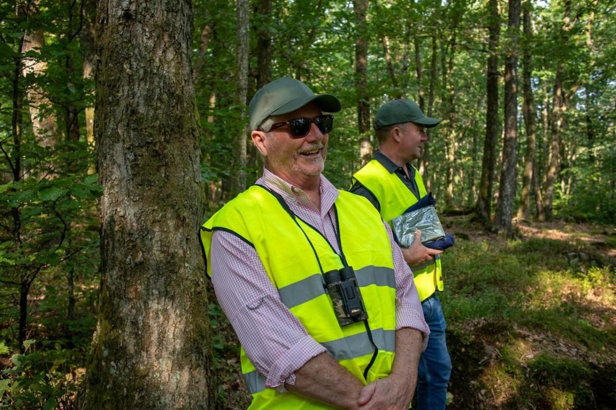 Two smiling people in high-cis vests in a forested area.