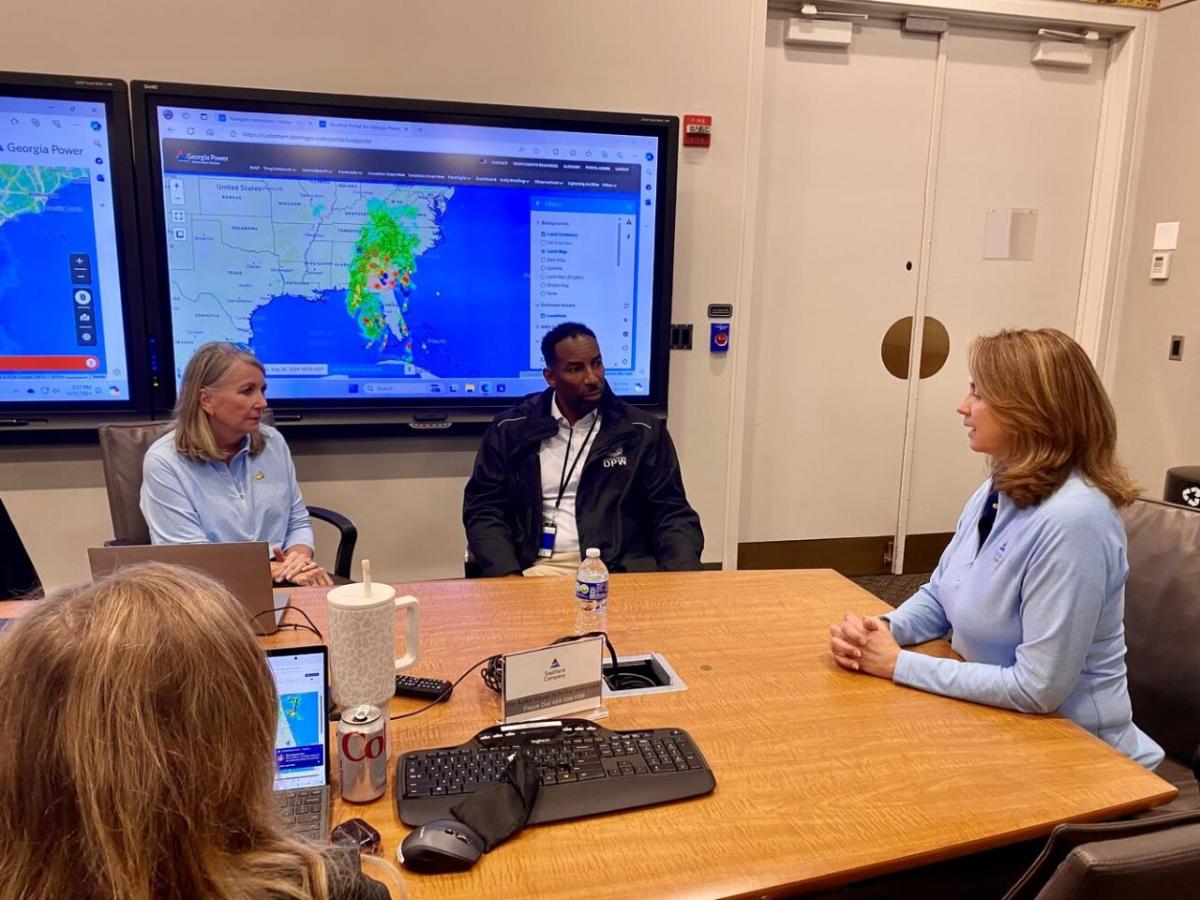 People meeting in a conference room. Digital screens with maps of the hurricane area displayed.