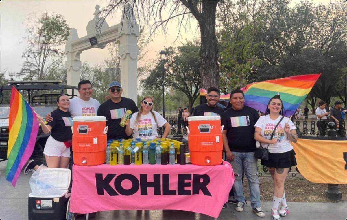 People standing behind a booth with Kohler banner and rainbow flags.