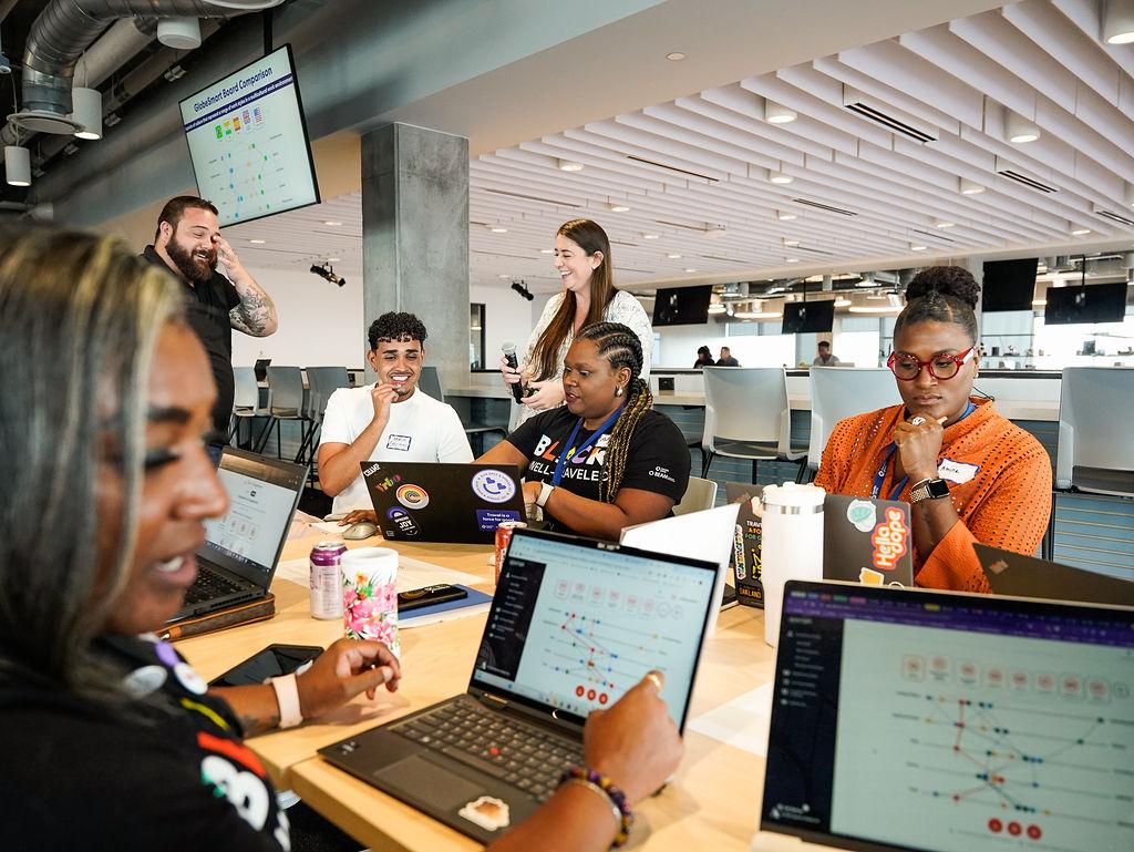 A small group seated at a table, each with a laptop open, talking together.