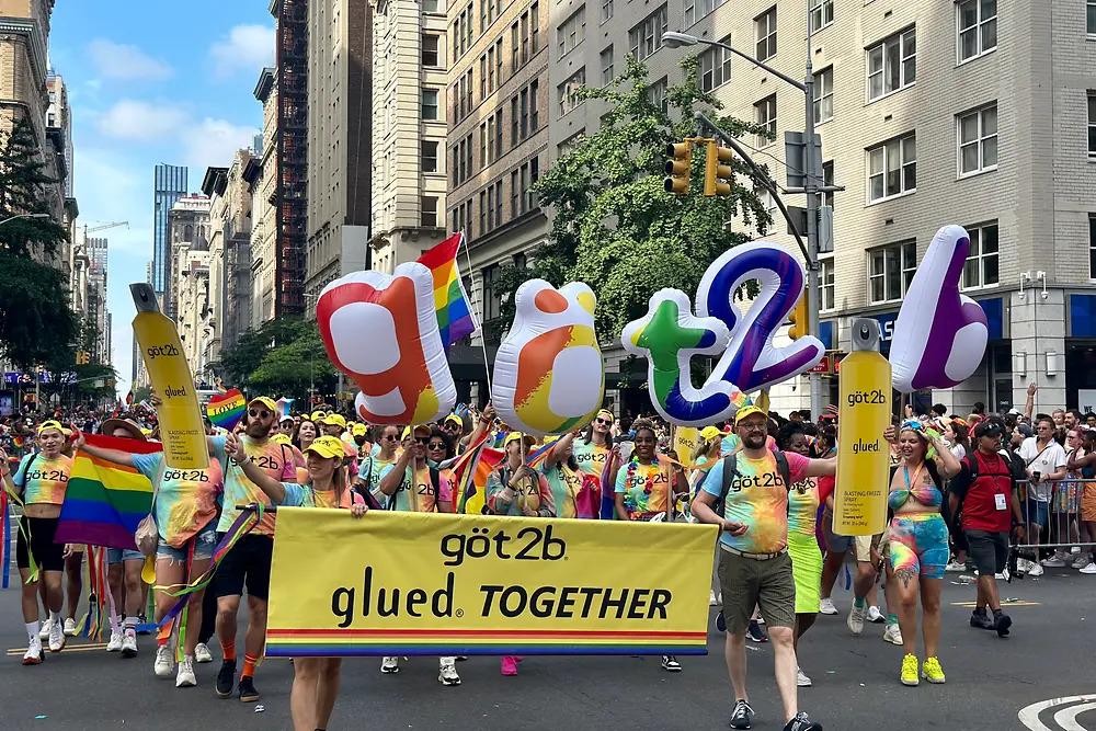 People marching down a street with balloons and a banner "got2b glued together".