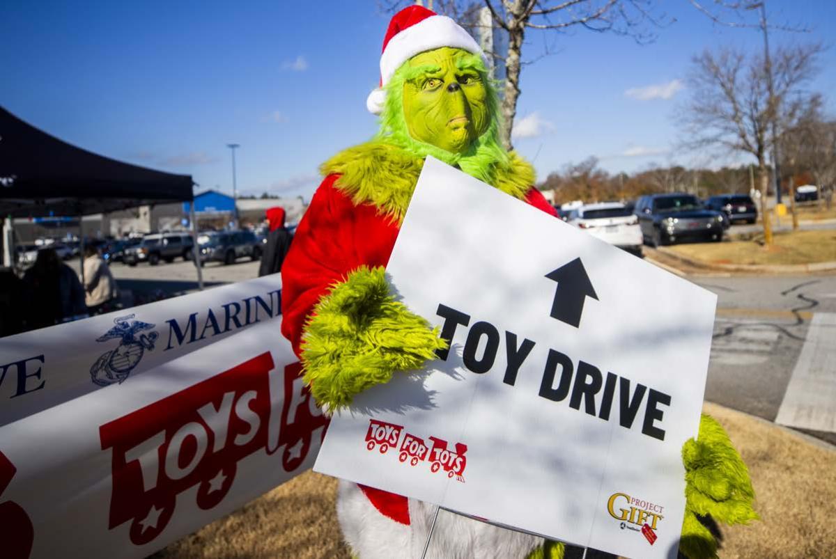 A person dressed as the Grinch holding a sign "Toy Drive" outside.