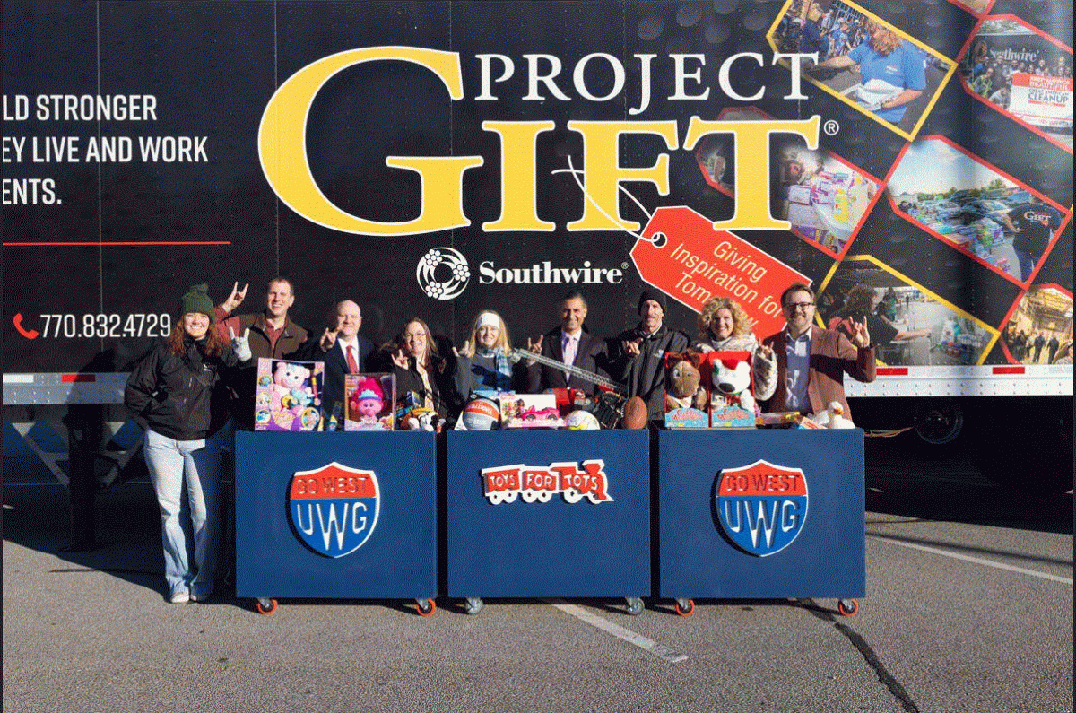 A group posed in front of a semi trailer. A table in front of them with toys on it.