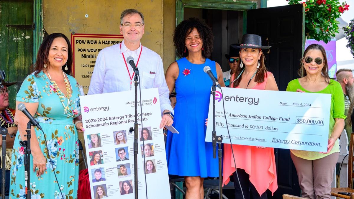 Five people posed with a large check and profiles of scholarship winners.