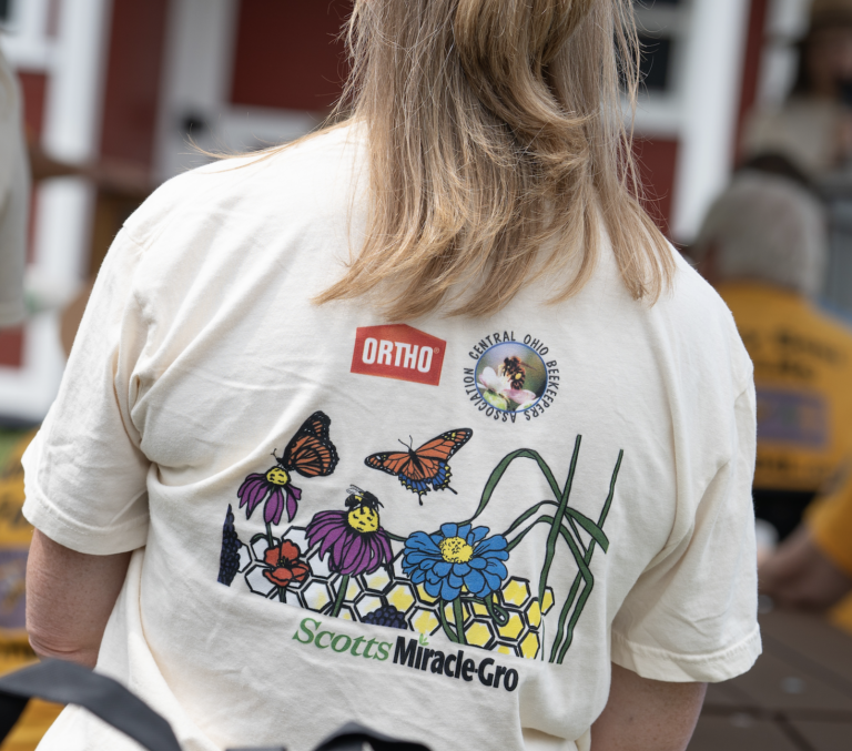 The back of a person's shirt with wildflowers and butterflies and the Ortho and ScottsMiracleGro logos.