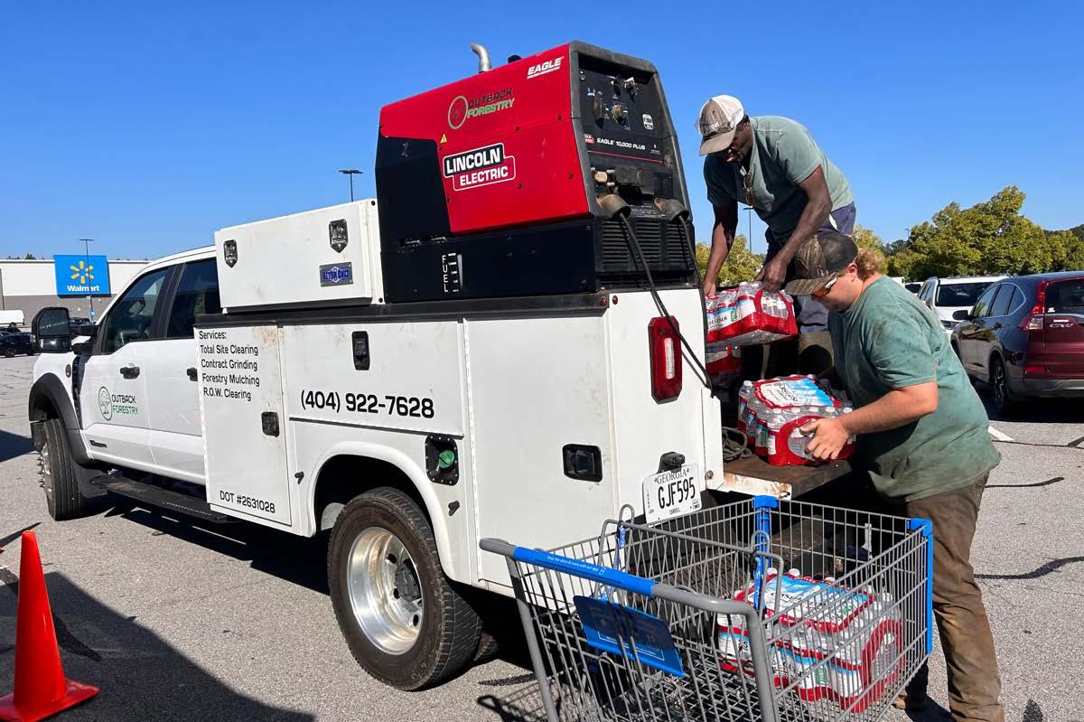 People loading water bottles into a cart from a truck in a parking lot.