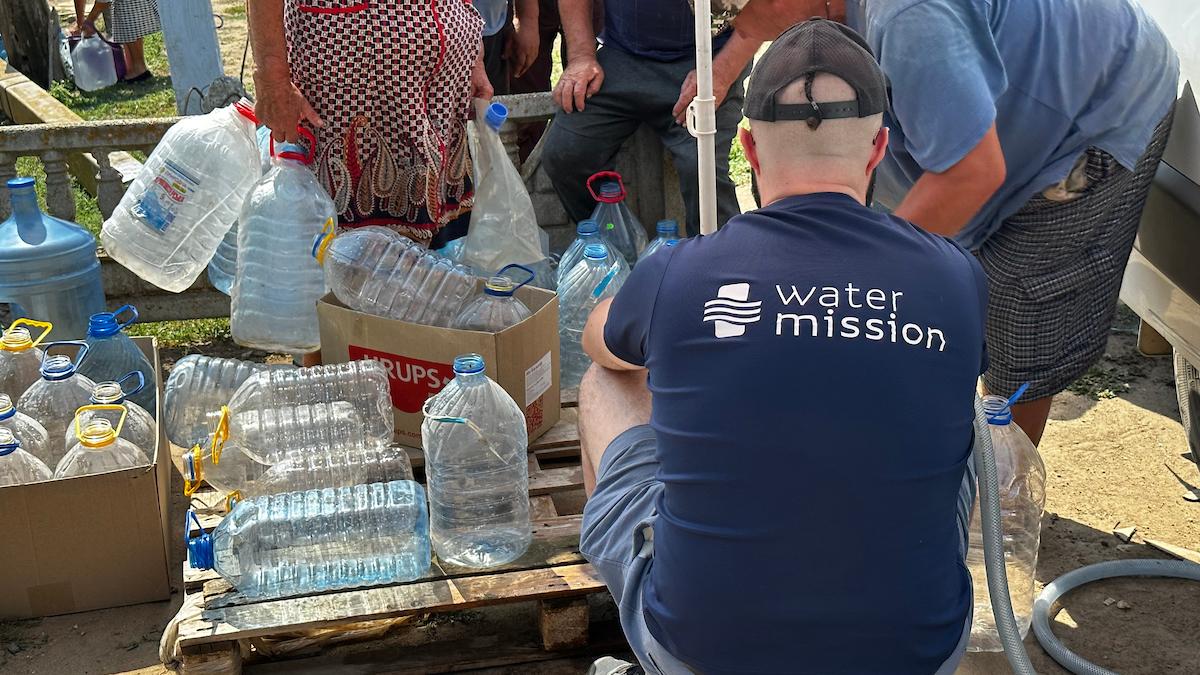 A person in a water mission shirt helping others fill plastic bottles.