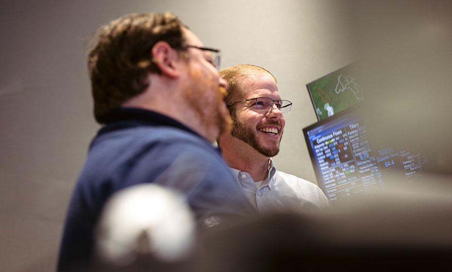 Two people smiling and looking at screens